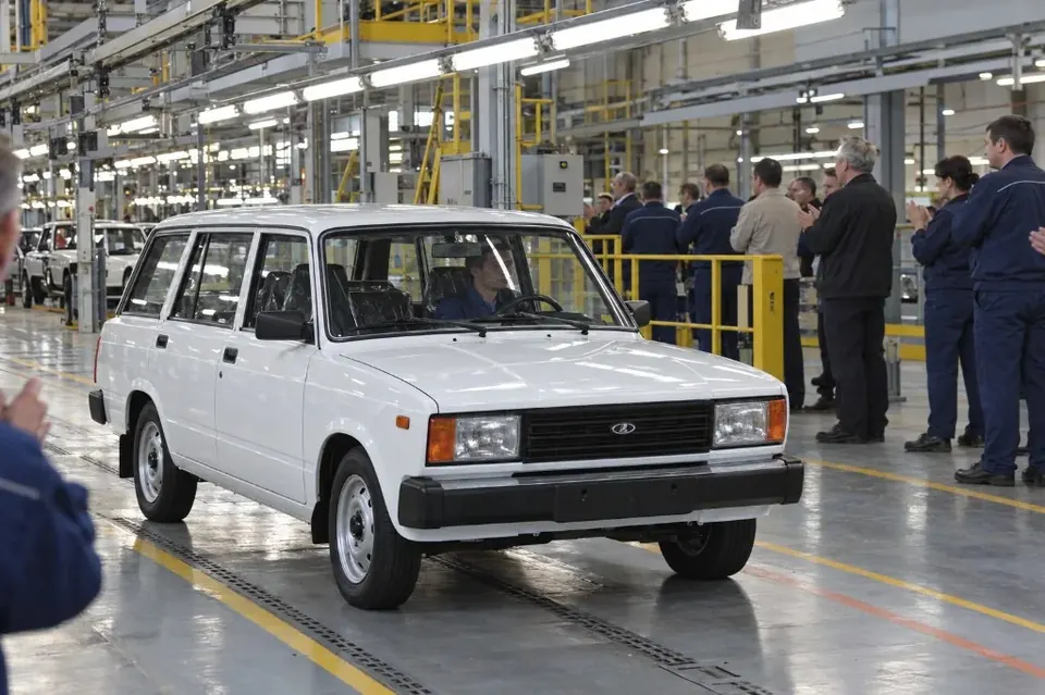 Белый универсал LADA 2104 выезжает из цеха, рабочие в синих комбинезонах провожают его аплодисментами